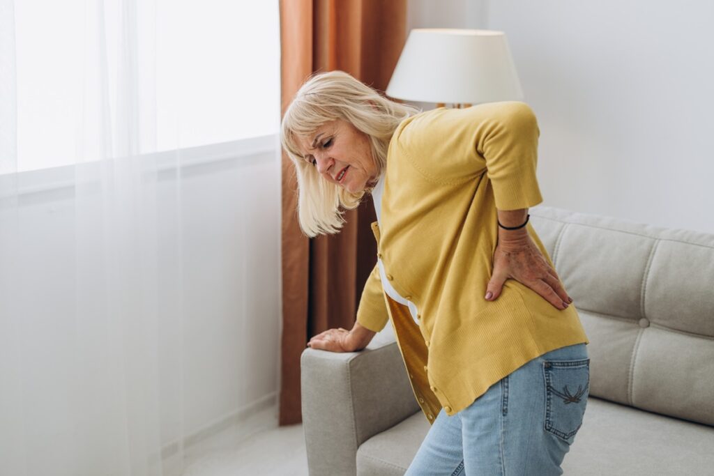 Senior woman having backache and touching her back in living roo