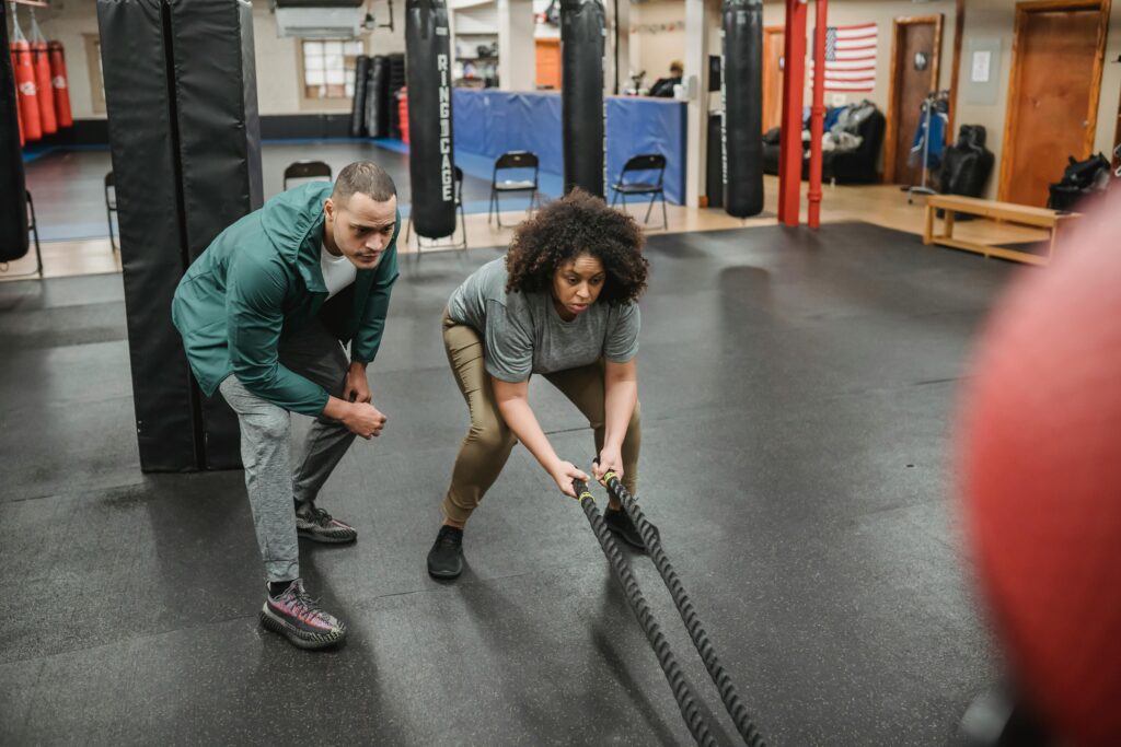 Man coaching a woman using battle ropes as part of a hypertrophy training program to increase muscle endurance and strength