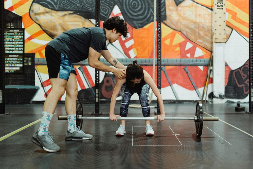 Man guiding a woman through proper deadlift form as part of a hypertrophy training program to build muscle and strength