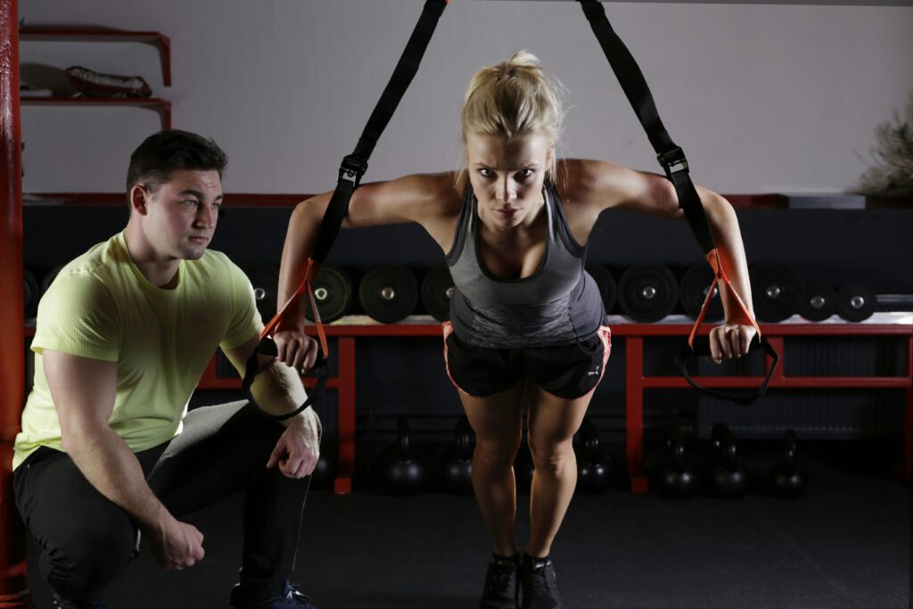 Man guiding a woman performing suspended push-ups with ropes, demonstrating an advanced bodyweight strength training exercise